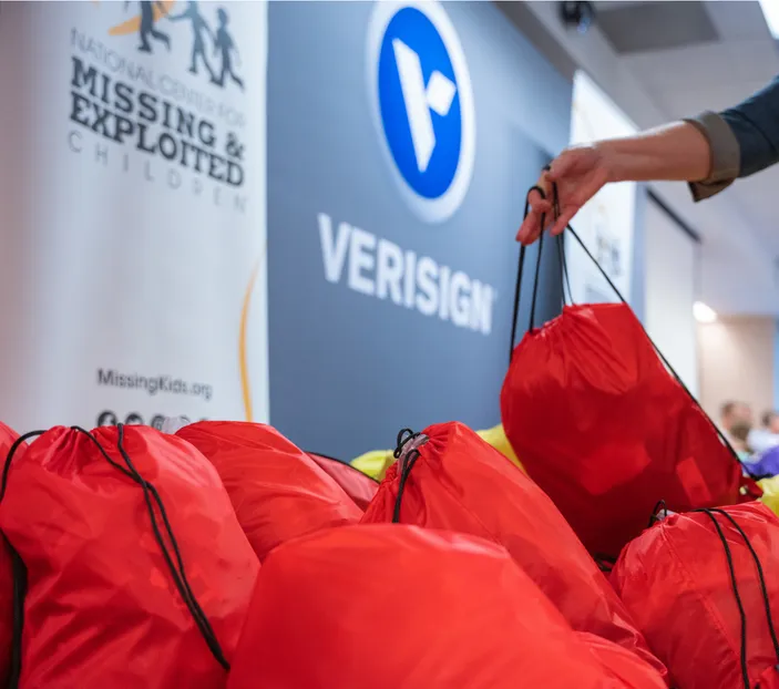Red and yellow backpacks full of supplies set down under a Verisign and National Center for Missing and Exploited Children logos.